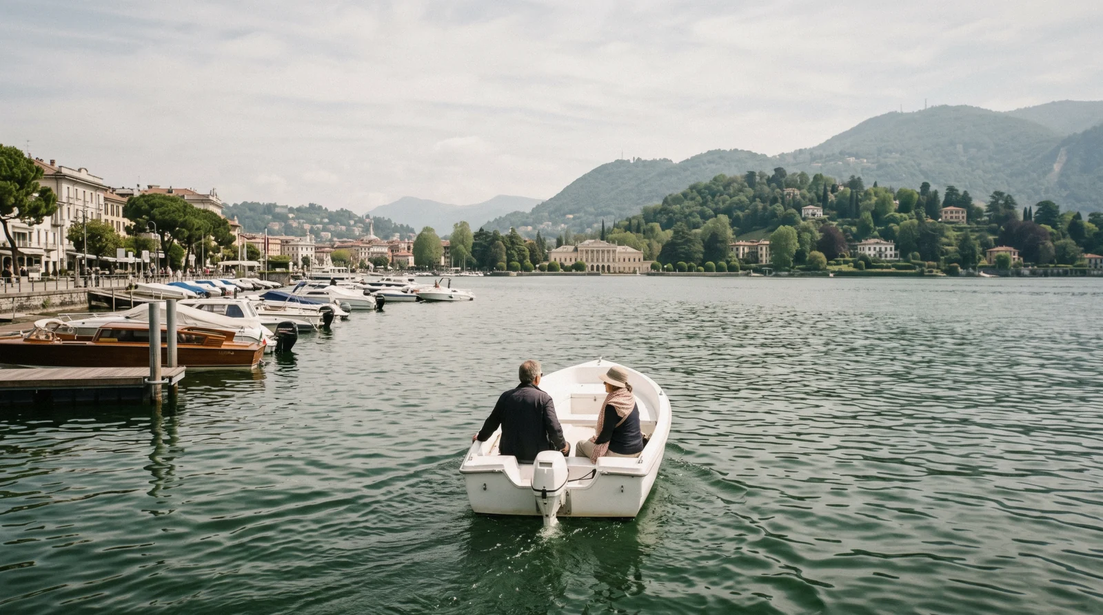 A small open motorboat idling off the Como lakefront with Villa Olmo shore behind, boat rental in Como