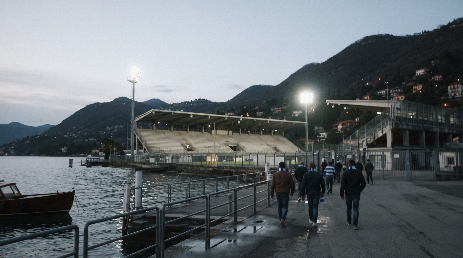 Floodlights on at the lakeside Stadio Giuseppe Sinigaglia at dusk with fans walking to the gates, the ground Como 1907 tickets are sold for