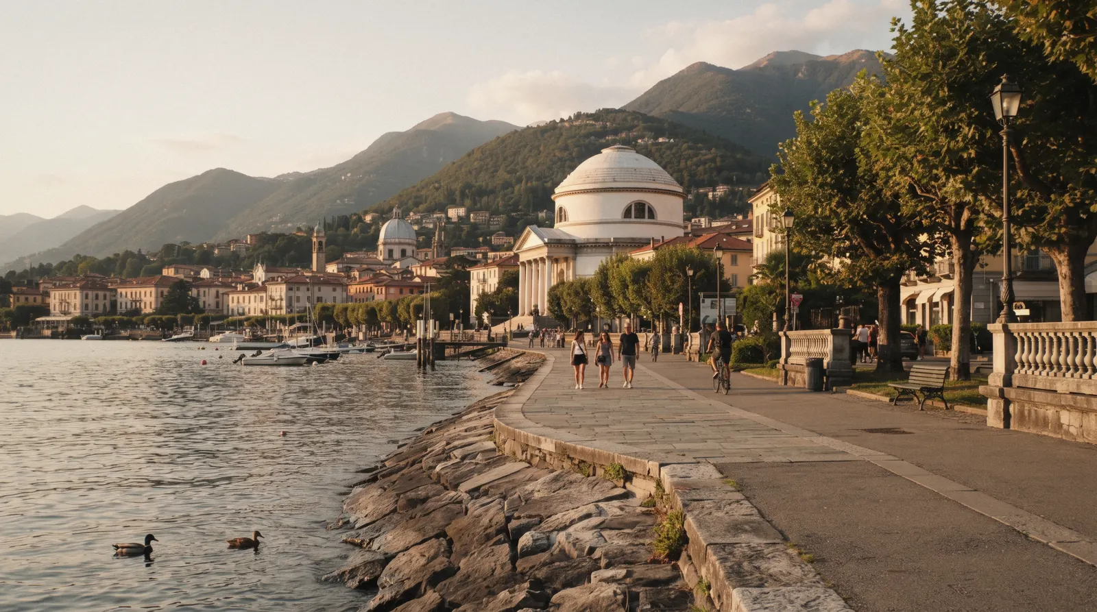 Walkers and cyclists on the Como waterfront promenade with the lake and hills behind in Como, Italy