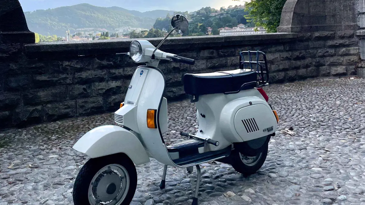 A classic cream-colored Vespa parked on a cobbled street on a Lake Como Vespa rental tour in Como, Italy